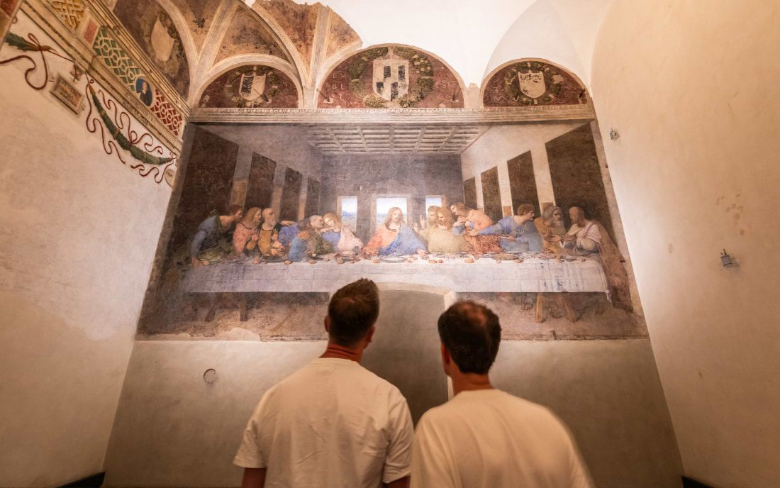 Two visitors standing before Leonardo da Vinci's The Last Supper mural in the refectory of Santa Maria delle Grazie, Milan