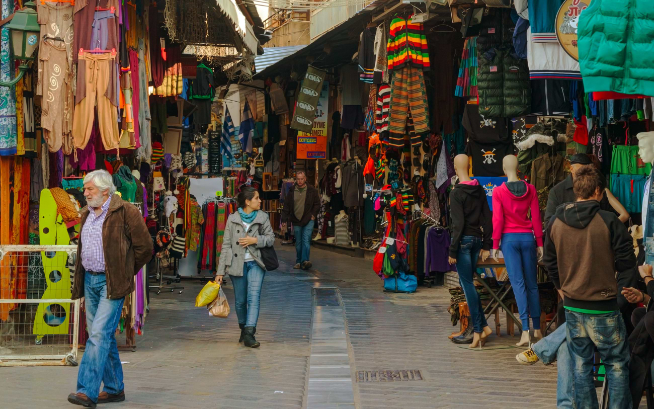 Shoppers browsing colourful clothing stalls hanging with garments in the busy Monastiraki street market in Athens