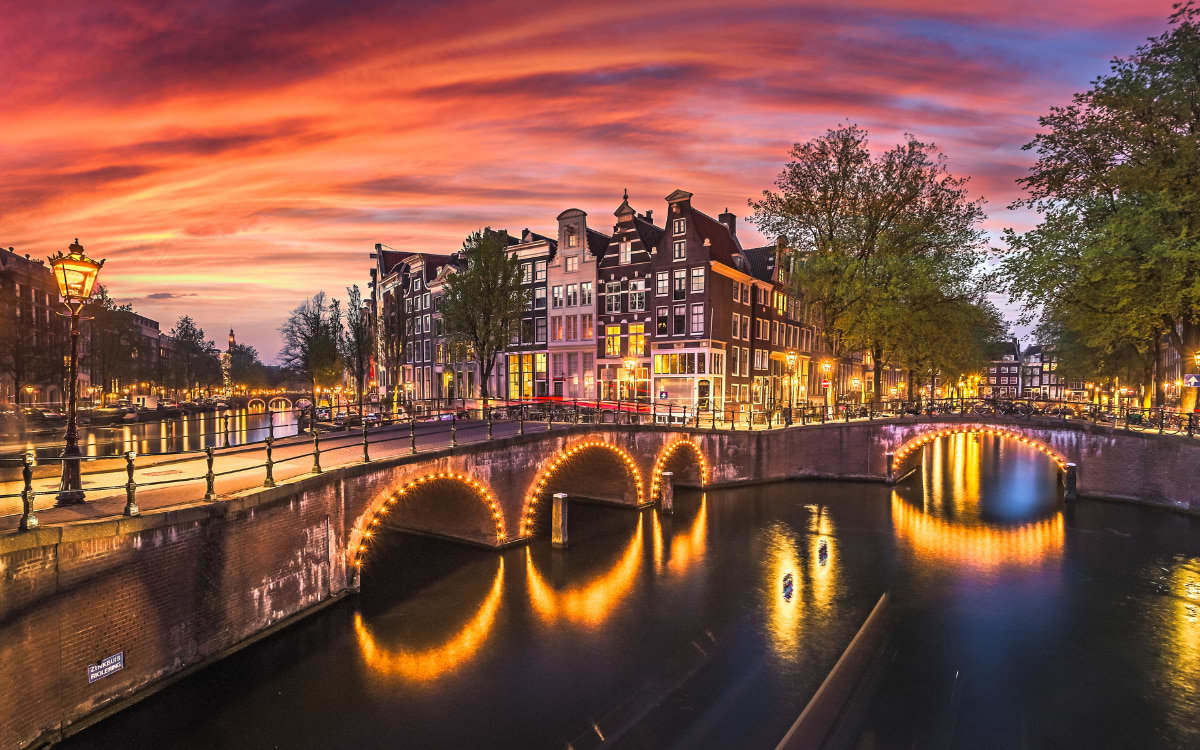 Beleuchtete Grachtenbrücken in Amsterdam bei Sonnenuntergang, romantisches Stadtbild bei Nacht