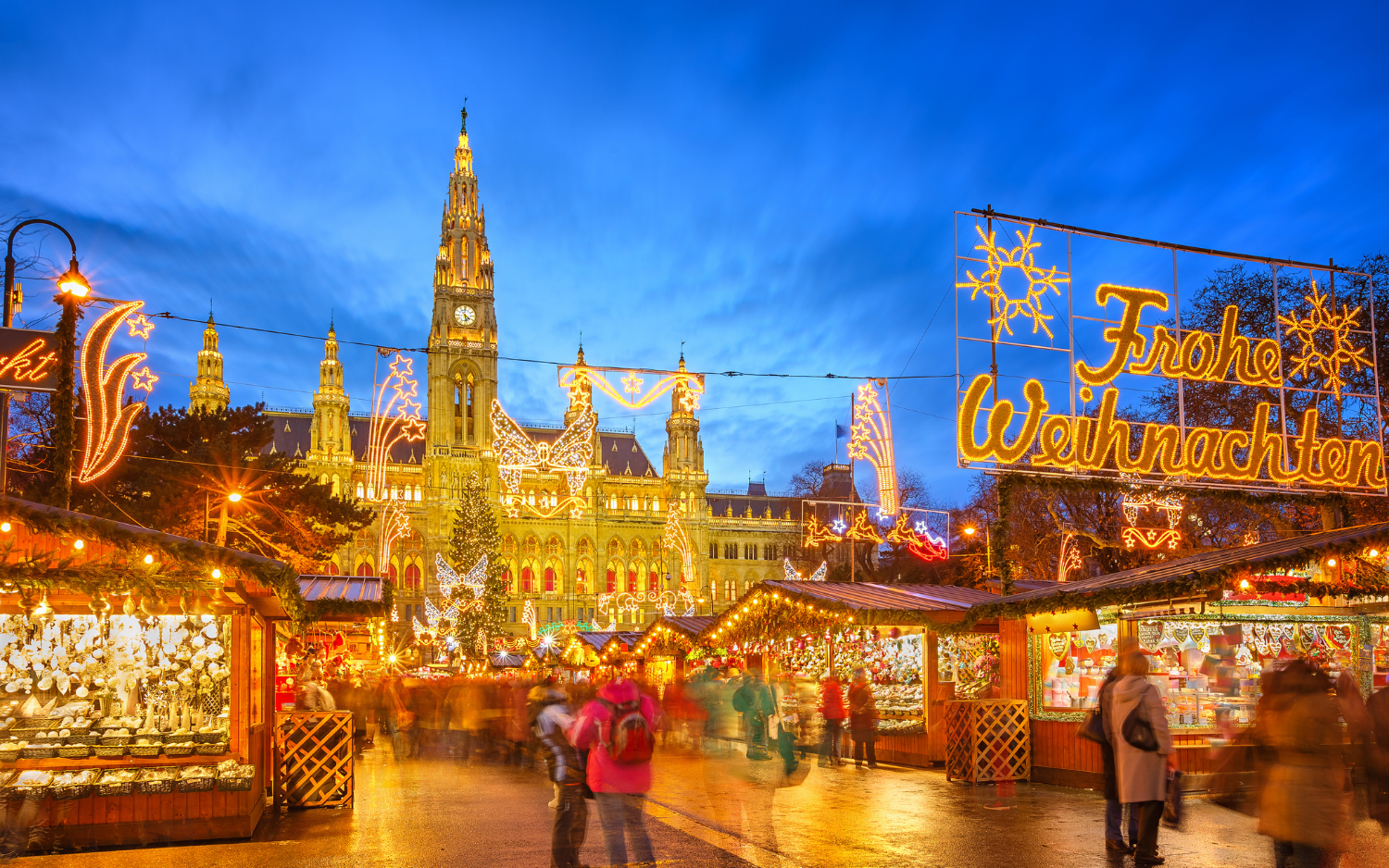 Vienna Christmas market at Rathausplatz with a glowing Frohe Weihnachten sign and the illuminated neo-Gothic City Hall