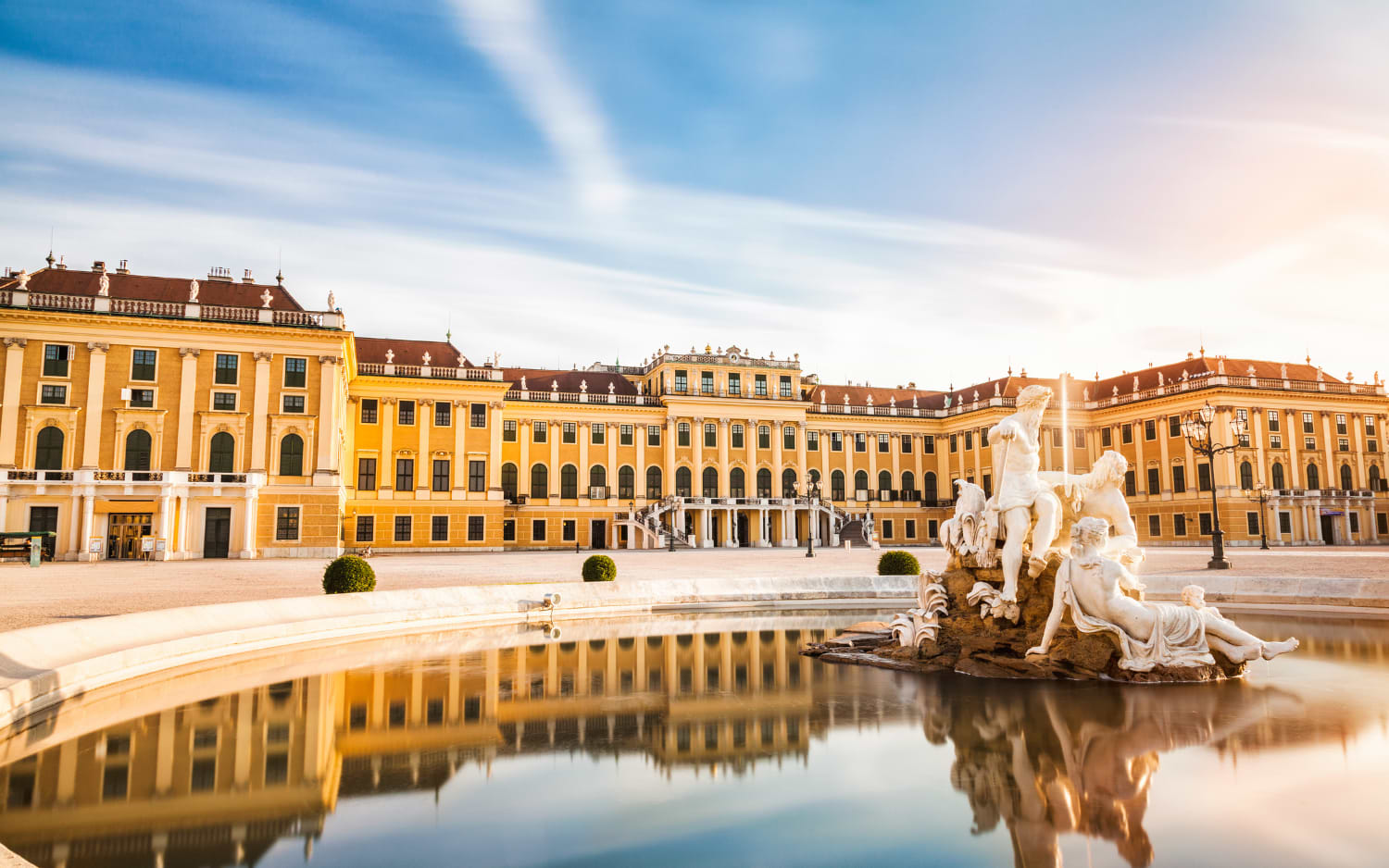 Schönbrunn Palace in Vienna, yellow Baroque facade at sunrise, reflected in a fountain with white marble statues