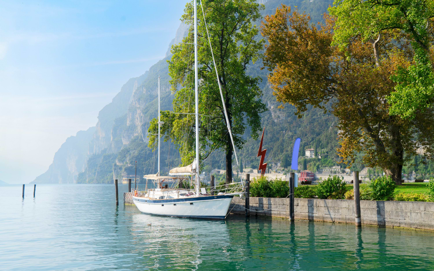 Segelboot am ruhigen türkisfarbenen Gardasee vor steil aufragenden Alpenfelsen im Hintergrund