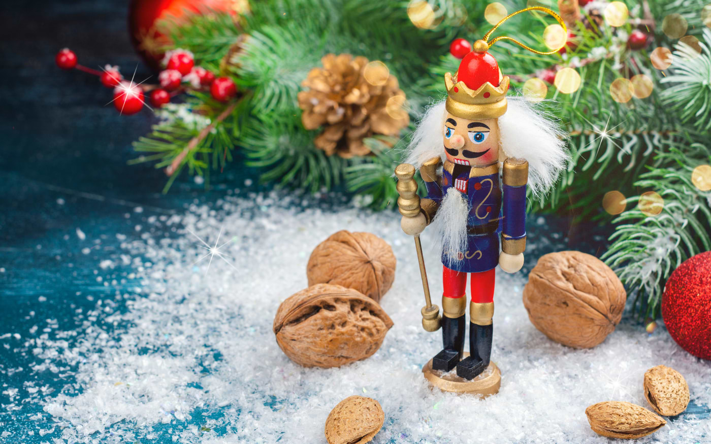 Wooden nutcracker figure wearing a crown standing among walnuts and almonds in snow