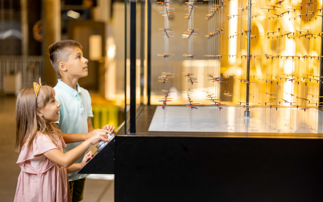 Two children interacting with an illuminated kinetic science exhibit at a science museum, Milan