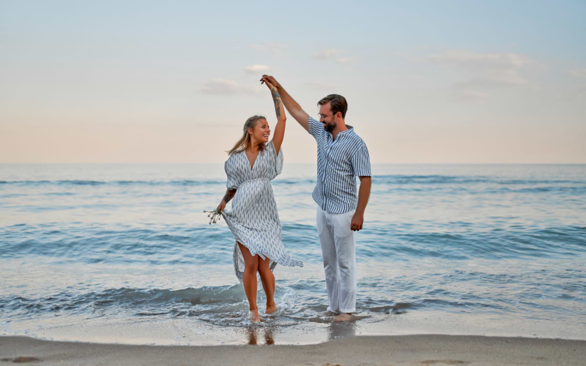 Couple dancing barefoot in the ocean waves at dusk on the beach in Rhodes, Greece