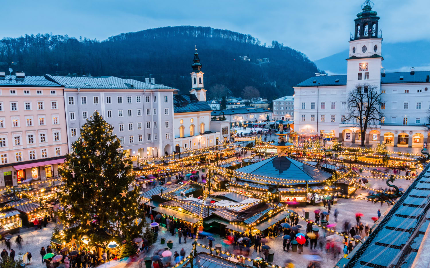 Salzburg Christkindlmarkt on Residenzplatz at dusk, with a decorated tree, lit stalls and the Glockenspiel tower