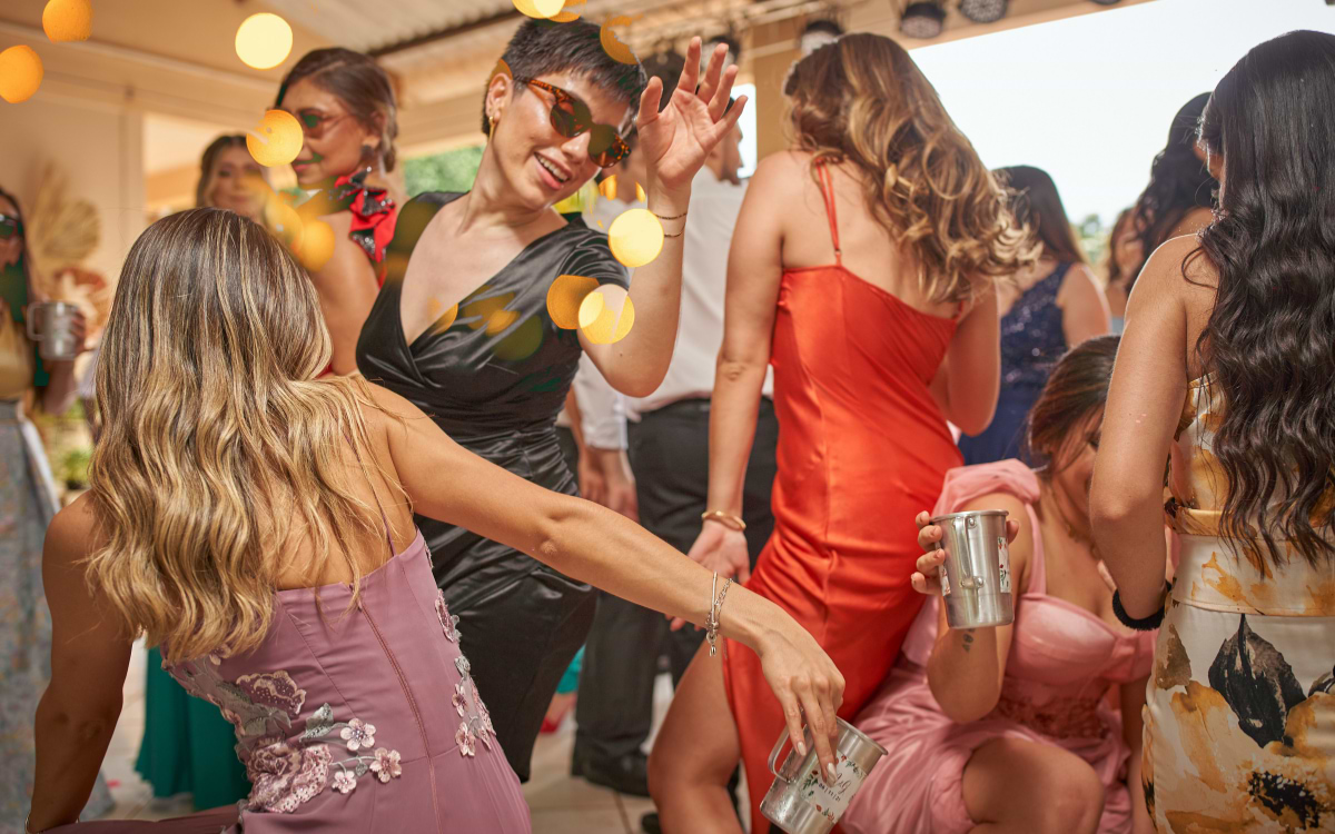 Women in elegant dresses dancing outdoors under string lights at a lively hen party celebration