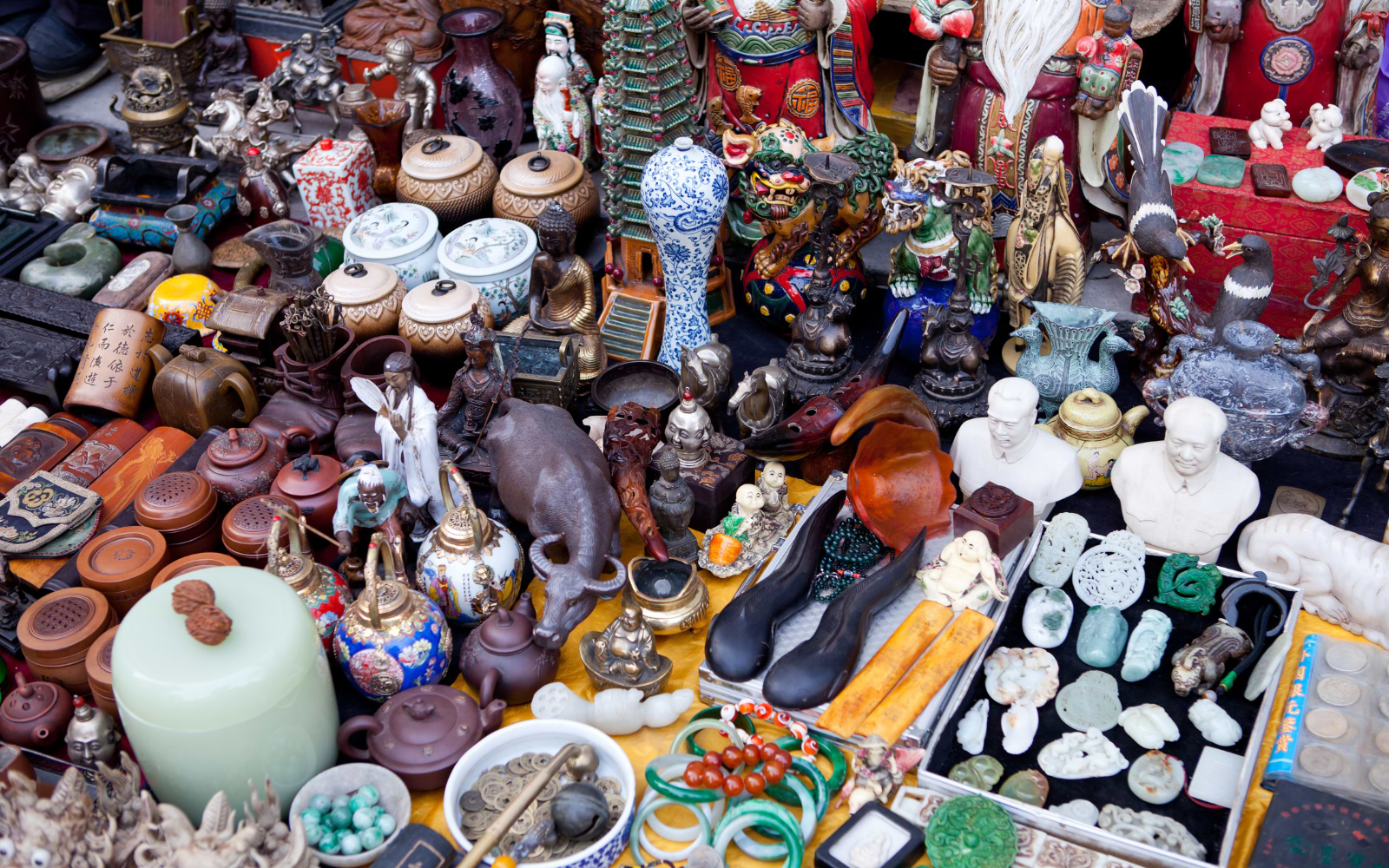 Flea market table crowded with antique porcelain, brass figures, jade carvings and old coins