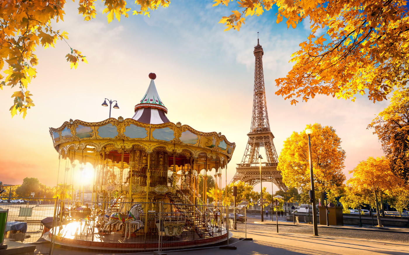 Vintage carousel near the Eiffel Tower in Paris at sunrise, framed by golden autumn trees along the street
