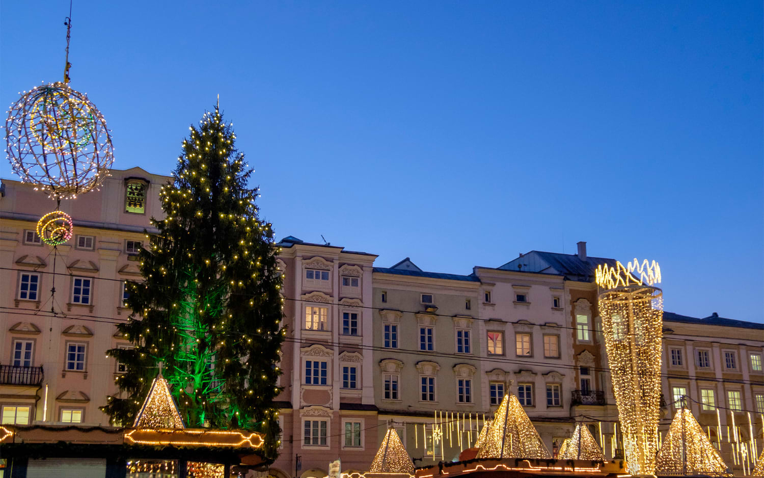 Lit Christmas tree, golden light pyramids and a giant light bauble in front of baroque town houses in Linz