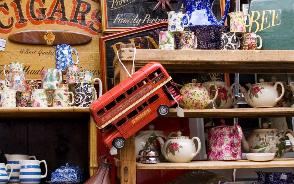 Shelves of floral English teapots and mugs with a red London double-decker bus model at a London flea market