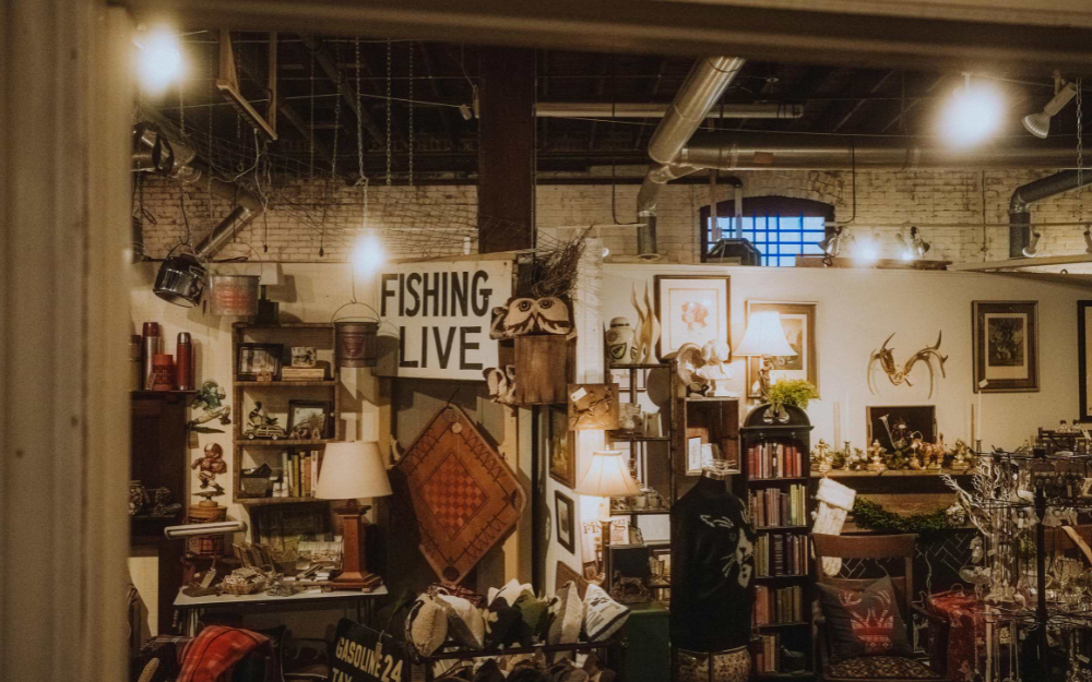 Indoor antique market stall displaying vintage lamps, framed art, rustic signs and eclectic collectibles