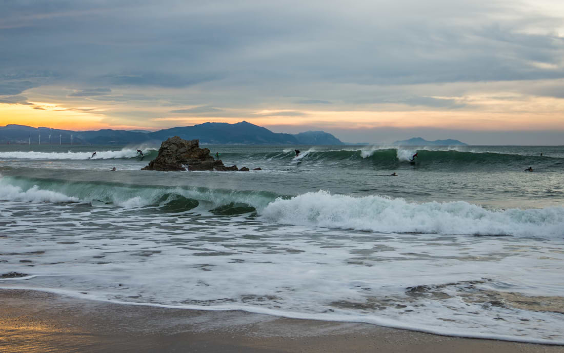 Surfers riding waves at sunset on the beach at Sopelana near Bilbao on the Bay of Biscay