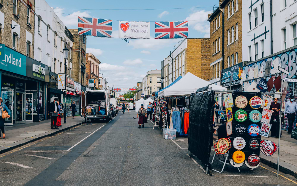 Portobello Road Market street scene with Union Jack flags, market stalls selling vintage signs and clothing in Notting Hill, London