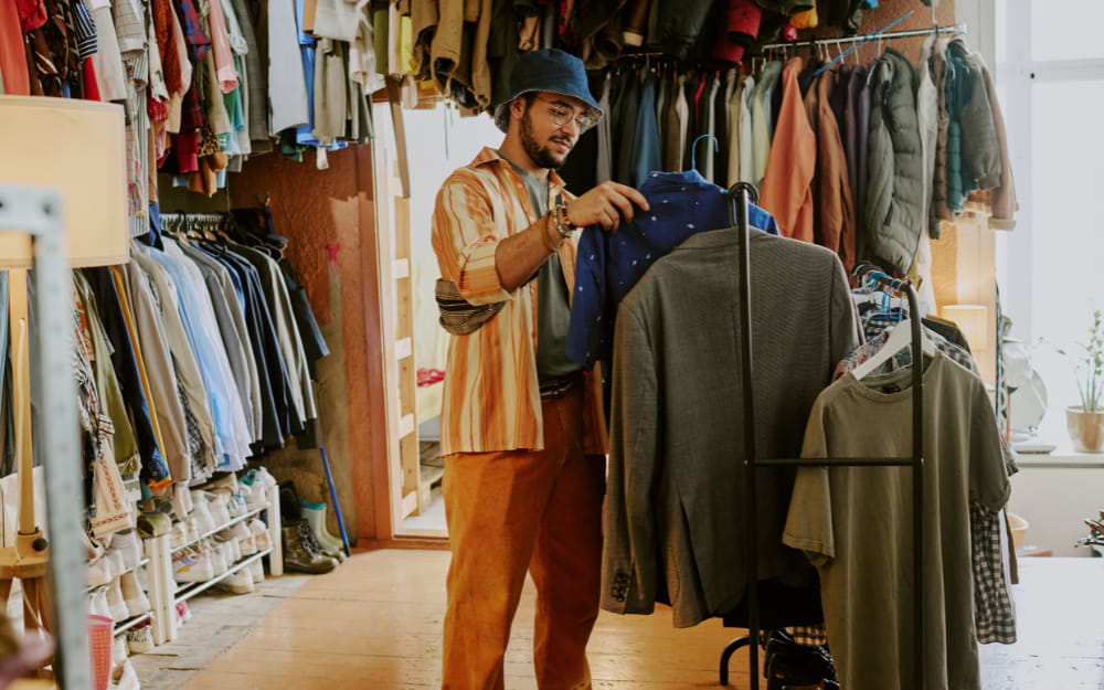 Man in a bucket hat browsing second-hand shirts and jackets at a vintage market in London