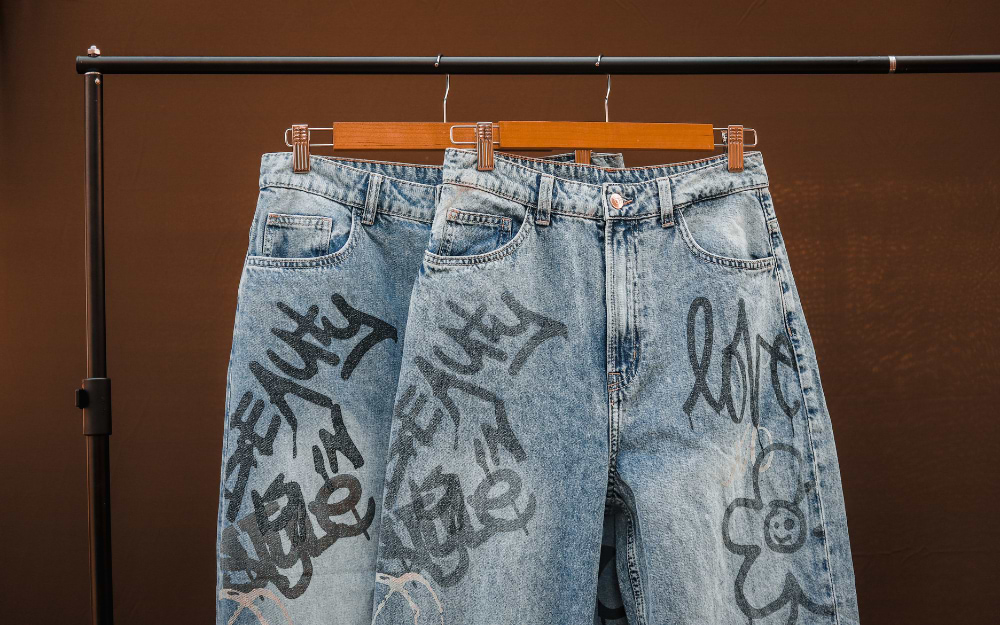 Graffiti-printed vintage denim jeans hanging on a rack at an Amsterdam flea market stall