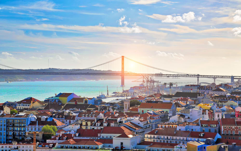 Sunset over Lisbon with the city skyline and the 25 de Abril Bridge in the background.