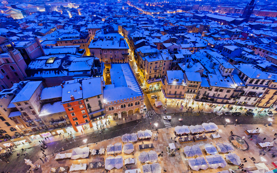 Festively decorated wooden stalls at Verona's Piazza dei Signori Christmas market, with visitors browsing handcrafted gifts and seasonal treats