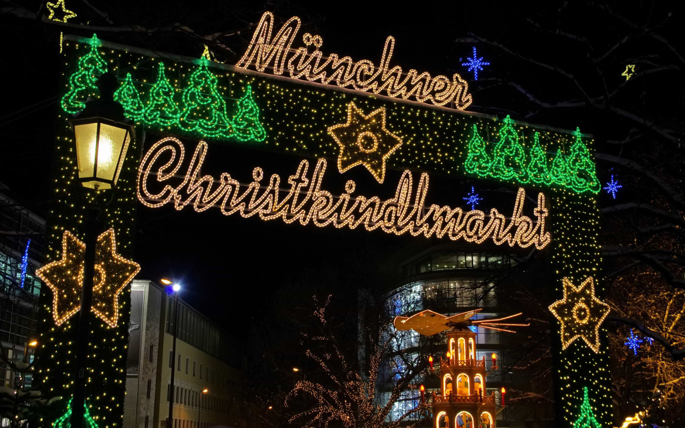 Illuminated Münchner Christkindlmarkt entrance arch with festive lights, stars and a Christmas pyramid at night in Munich