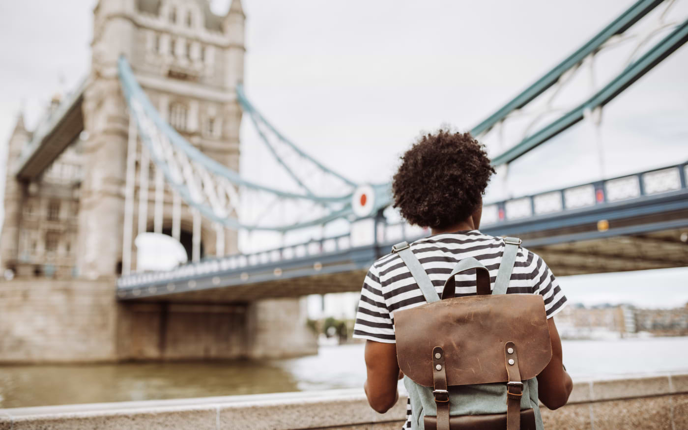 Traveller with a leather backpack and striped T-shirt looking at Tower Bridge from the Thames riverside in London